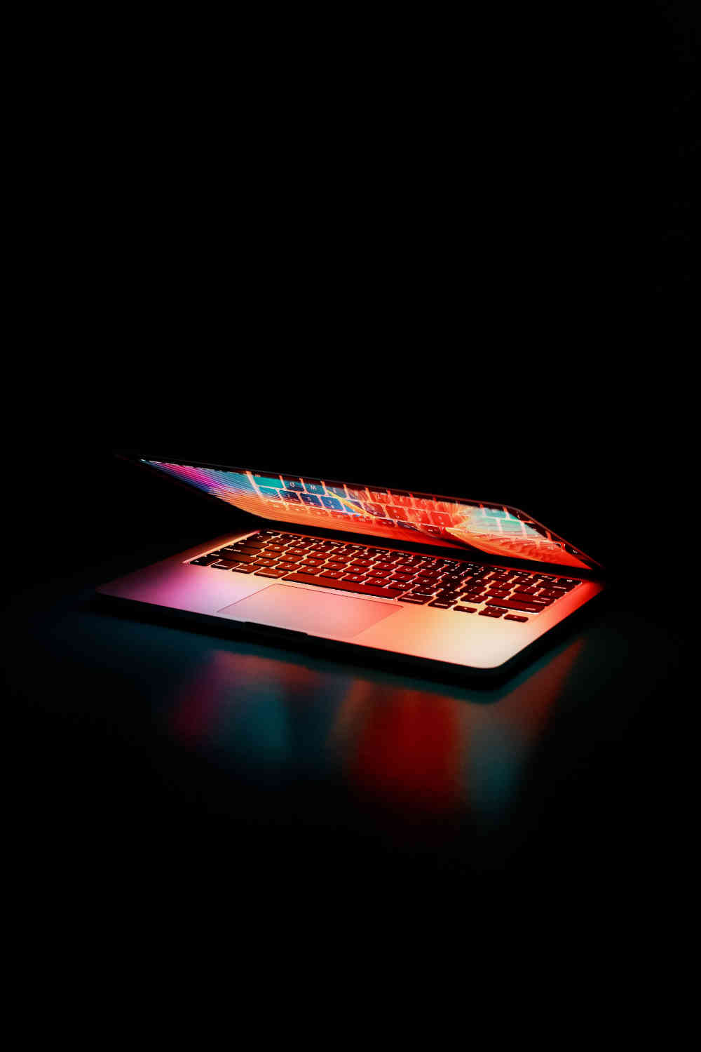 Semi-opened laptop emitting light, on black table with black background.